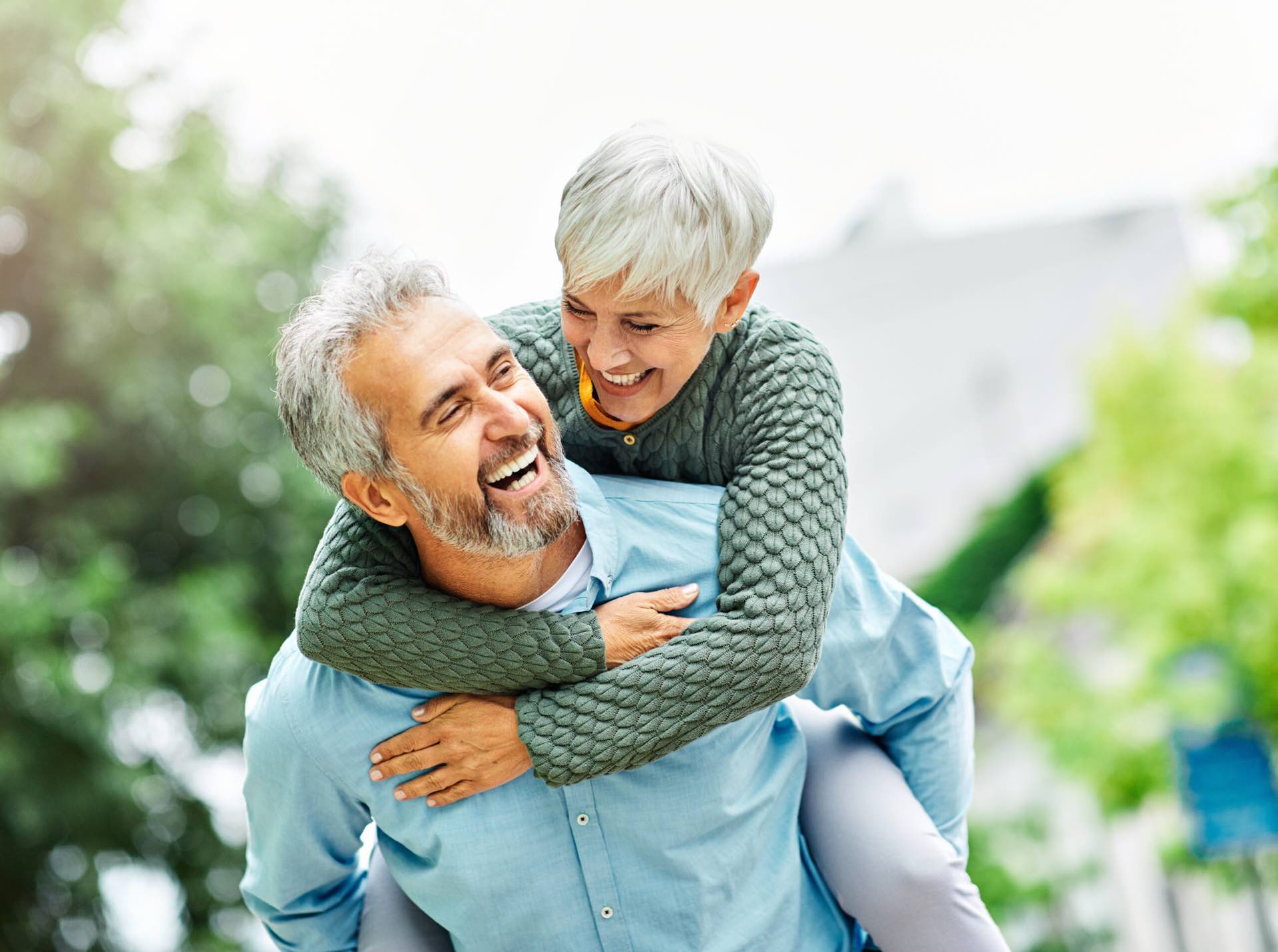 A smiling older man giving his partner a piggyback outdoors