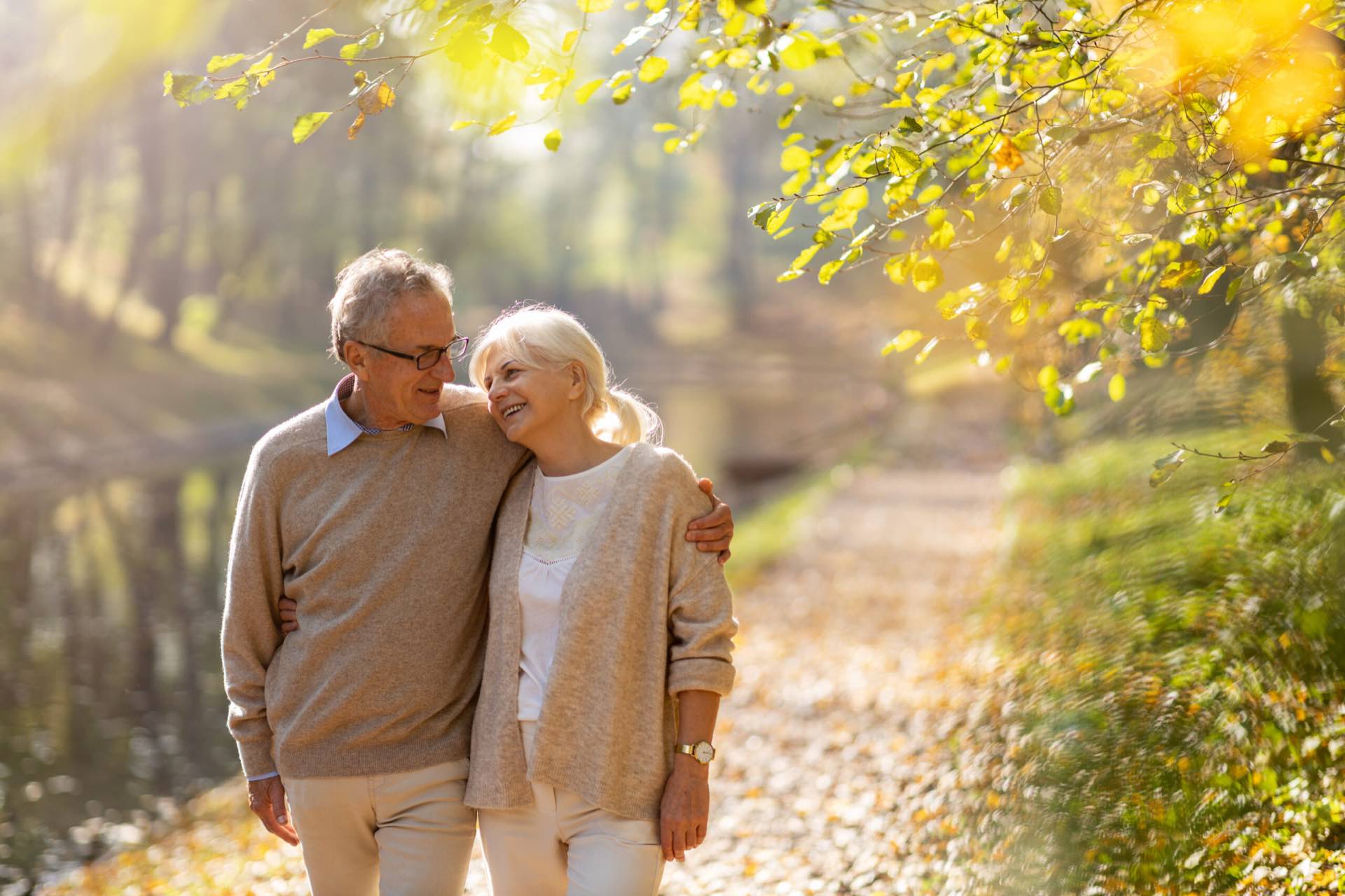 An older couple walking arm in arm along a woodland path