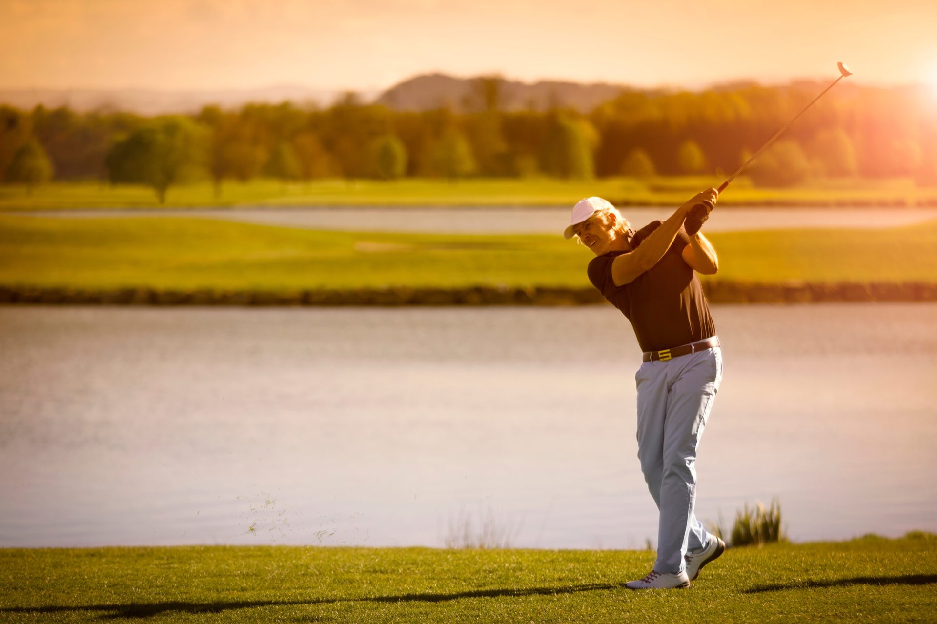 A golfer finishing his swing on a sunny golf course