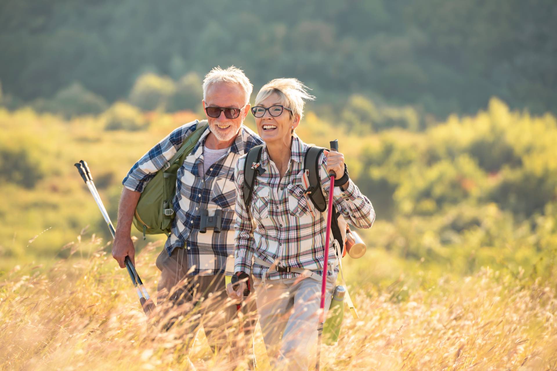 An older couple hiking with walking poles through long grass