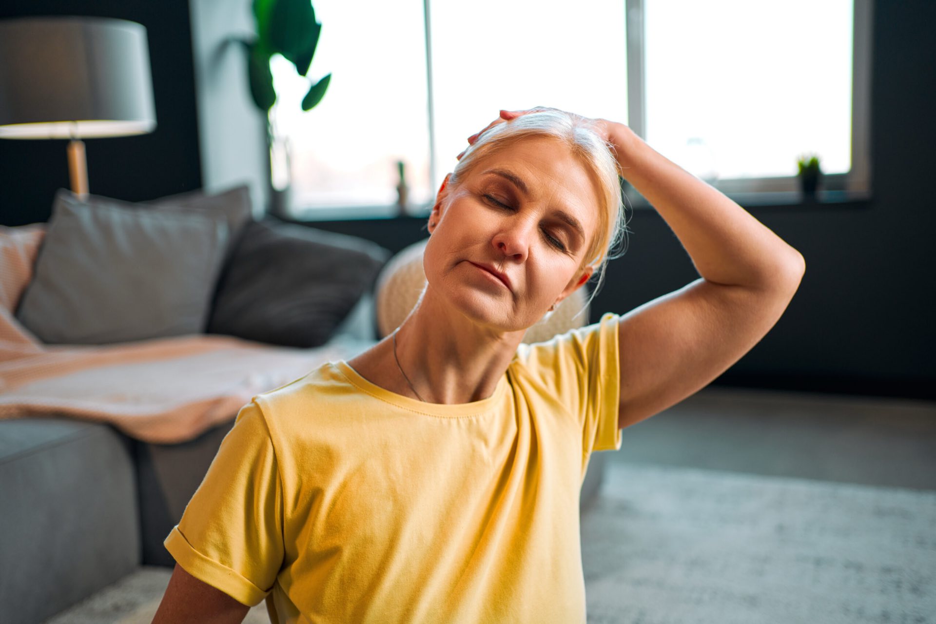 A woman at home stretching her neck to one side with her hand