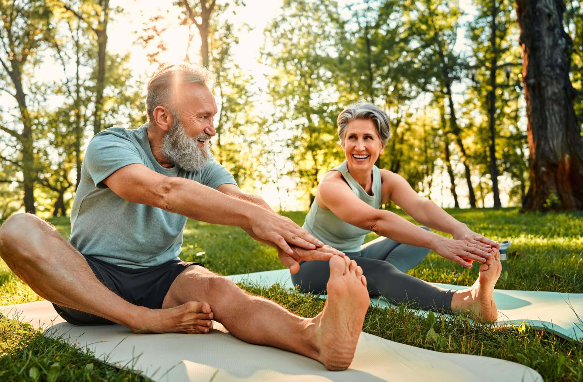 An older couple stretching their legs on mats in a sunny park