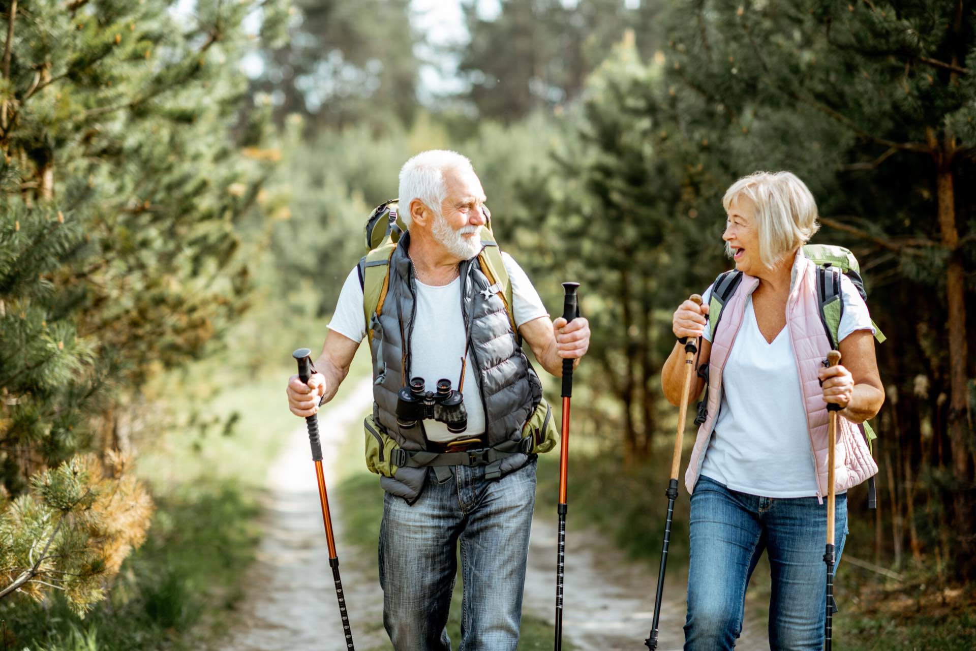 An older couple walking with hiking poles on a woodland trail