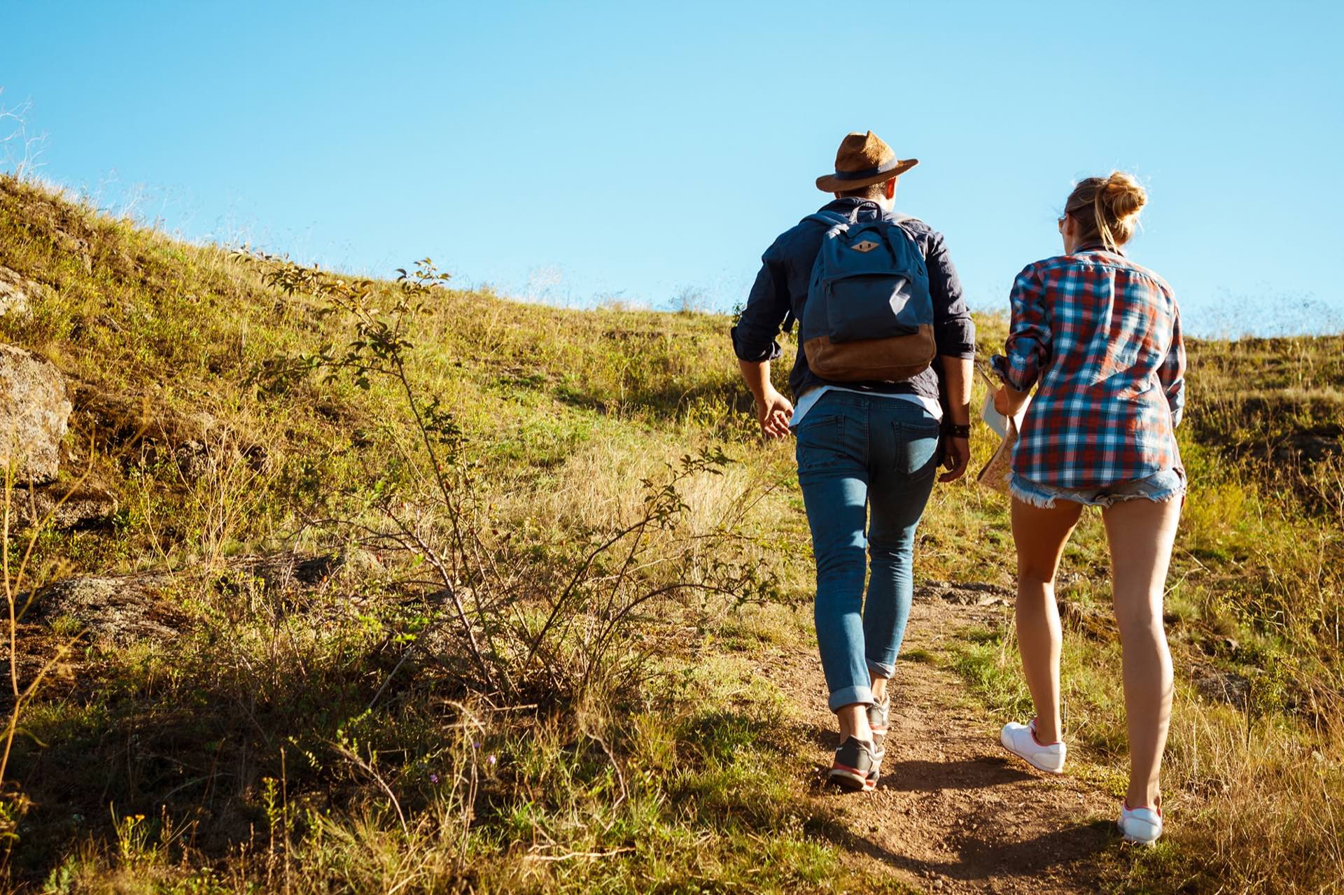 Two people walking up a grassy hillside path on a sunny day