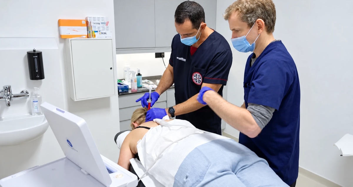 Two clinicians giving a patient a spinal injection while she lies face down