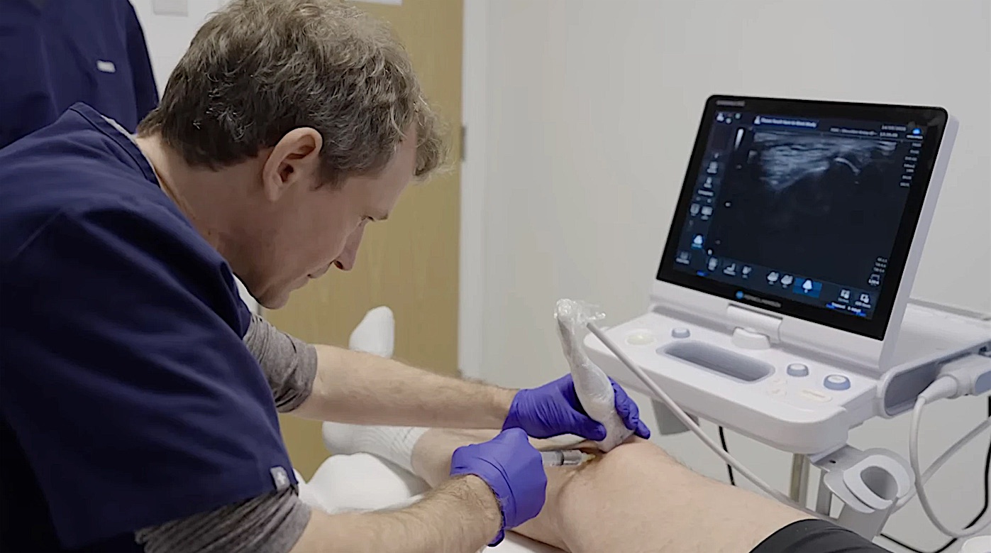 A clinician giving an injection into a patient’s knee under ultrasound guidance